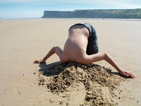 595131 young boy with head buried in sand on beach